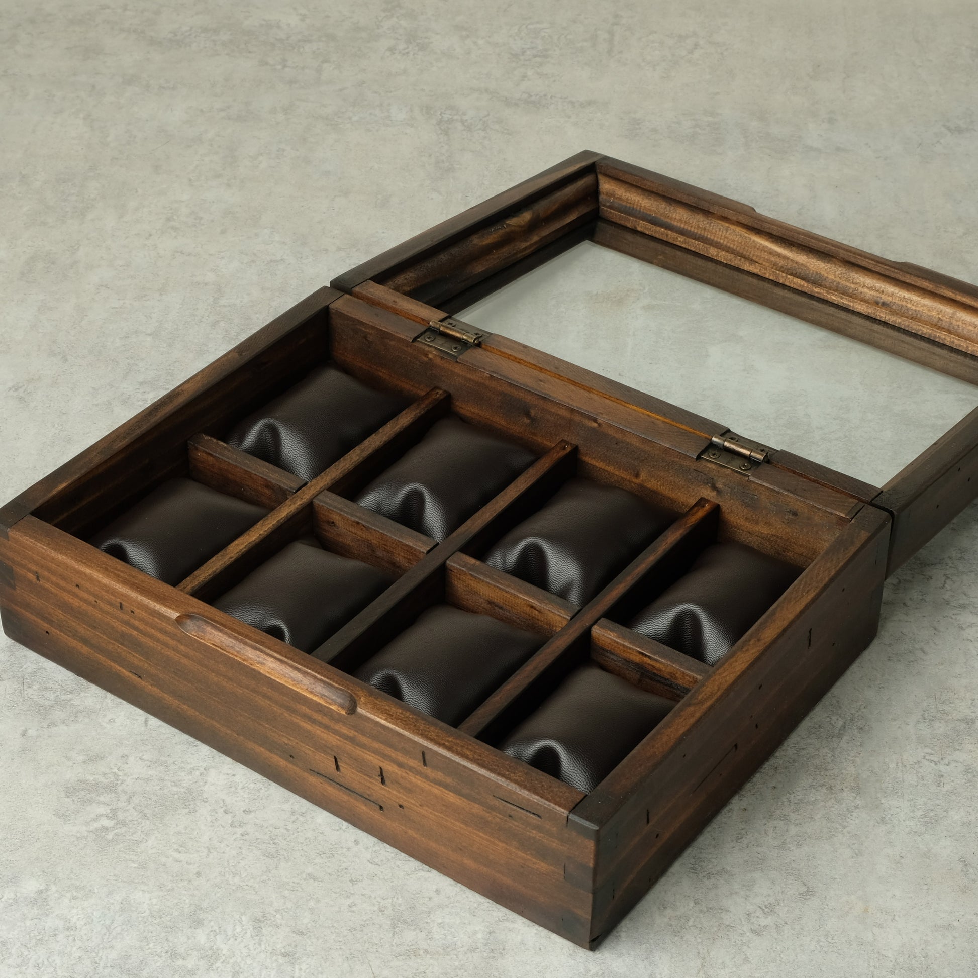 A dark brown wooden watch box with a hinged lid and eight individual watch slots lined