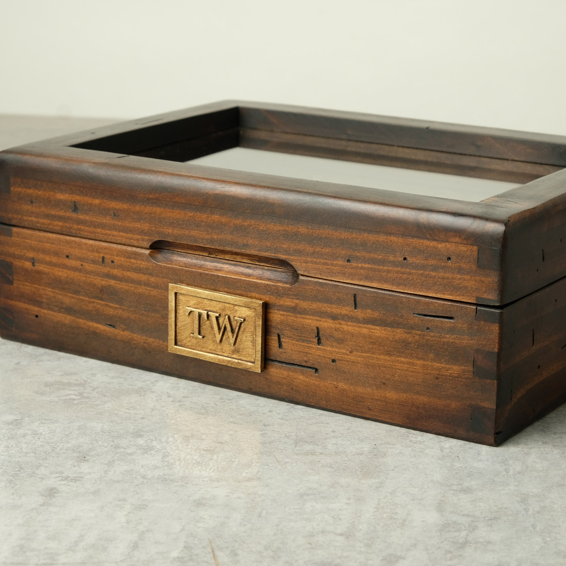A dark brown wooden display box with a glass top, featuring a brass monogrammed plate