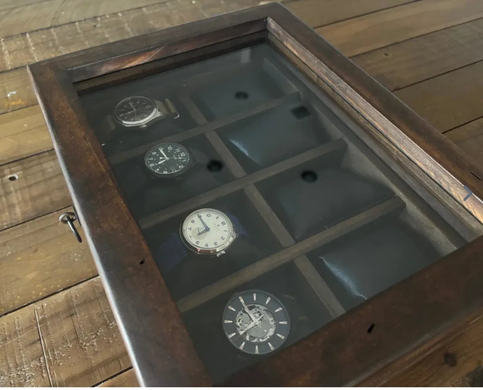 A close view through the glass lid of a handcrafted wooden watch box.
